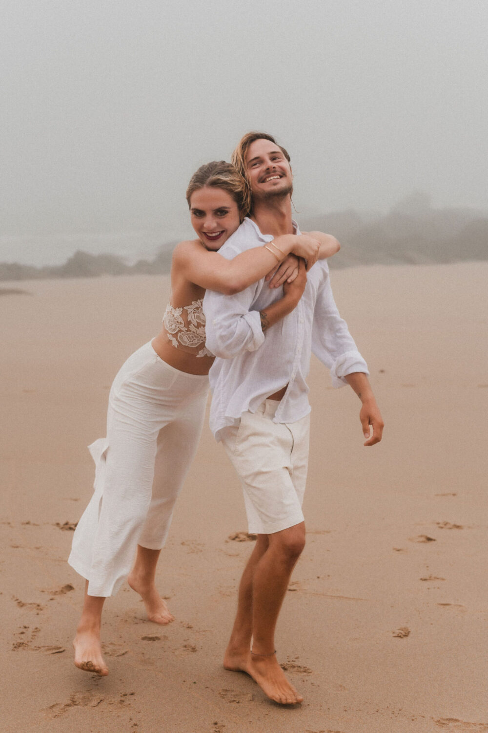 Deutsch: Braut umarmt Bräutigam von hinten am Strand Englisch: Bride hugs groom from behind on beach