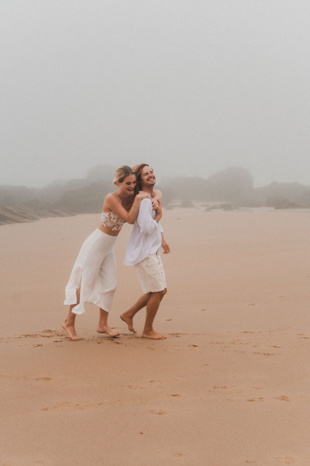 Deutsch: Braut und Bräutigam in weißen Outfits haben Spaß am Strand Englisch: Bride and groom in white outfits having fun on the beach