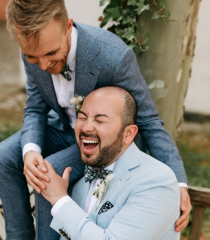 Deutsch: Lachendes schwules Hochzeitspaar in blauen Anzügen während Paarfotoshooting Englisch: Laughing gay wedding couple in blue suits during couple photoshoot